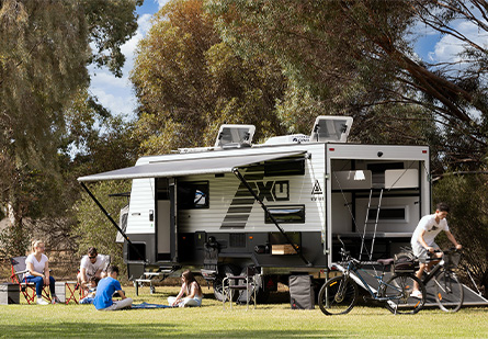 A family with their New Age Caravan camping setup, back toy hauler door open, man riding bike down the ramp.