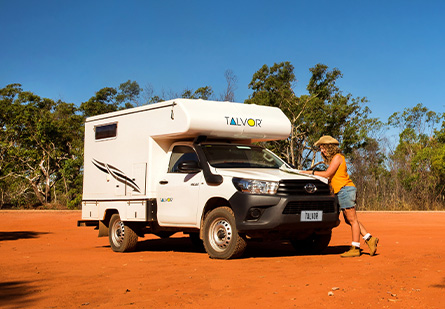 Talvor 4x4 Adventure Camper Ute Camper parked on some iconic red Australian dirt, bushland in the backgound. Woman leaning over the hood plotting a route on a map.