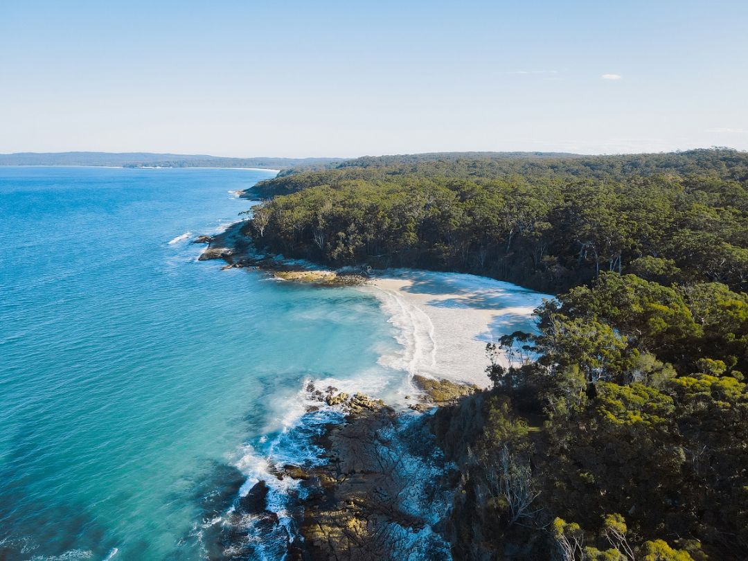 Secluded beach with crystal clear blue water, white sand, and lush green trees.