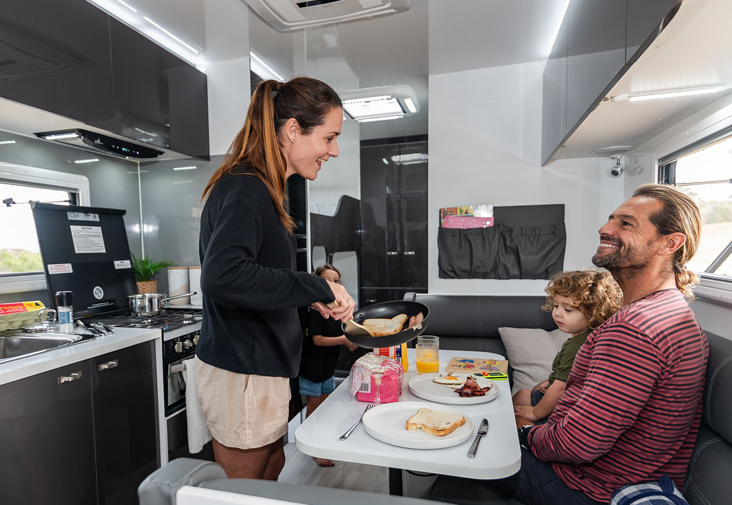 Family inside a caravan sitting and eating at the dinette, enjoying a meal together in a cozy space.