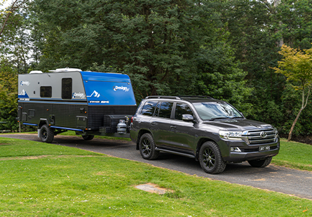 A dark grey SUV tows a sleek Design RV caravan on an open road. The caravan is ready for adventure, with a modern design and a spacious interior.