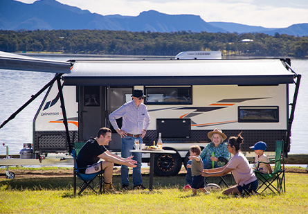 Family in front of a Windsor Genesis family model underneath the awning with a camping setup in front of a lake.