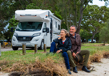 Older couple sitting in front of their parked Windsor Flinders motorhome.