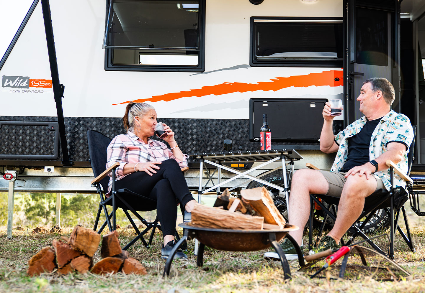 Couple sitting on chairs in front of a caravan, relaxing and enjoying the outdoor setting.