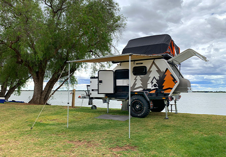 A Lumberjack Sheoak camper trailer set up in front of a waterfront.