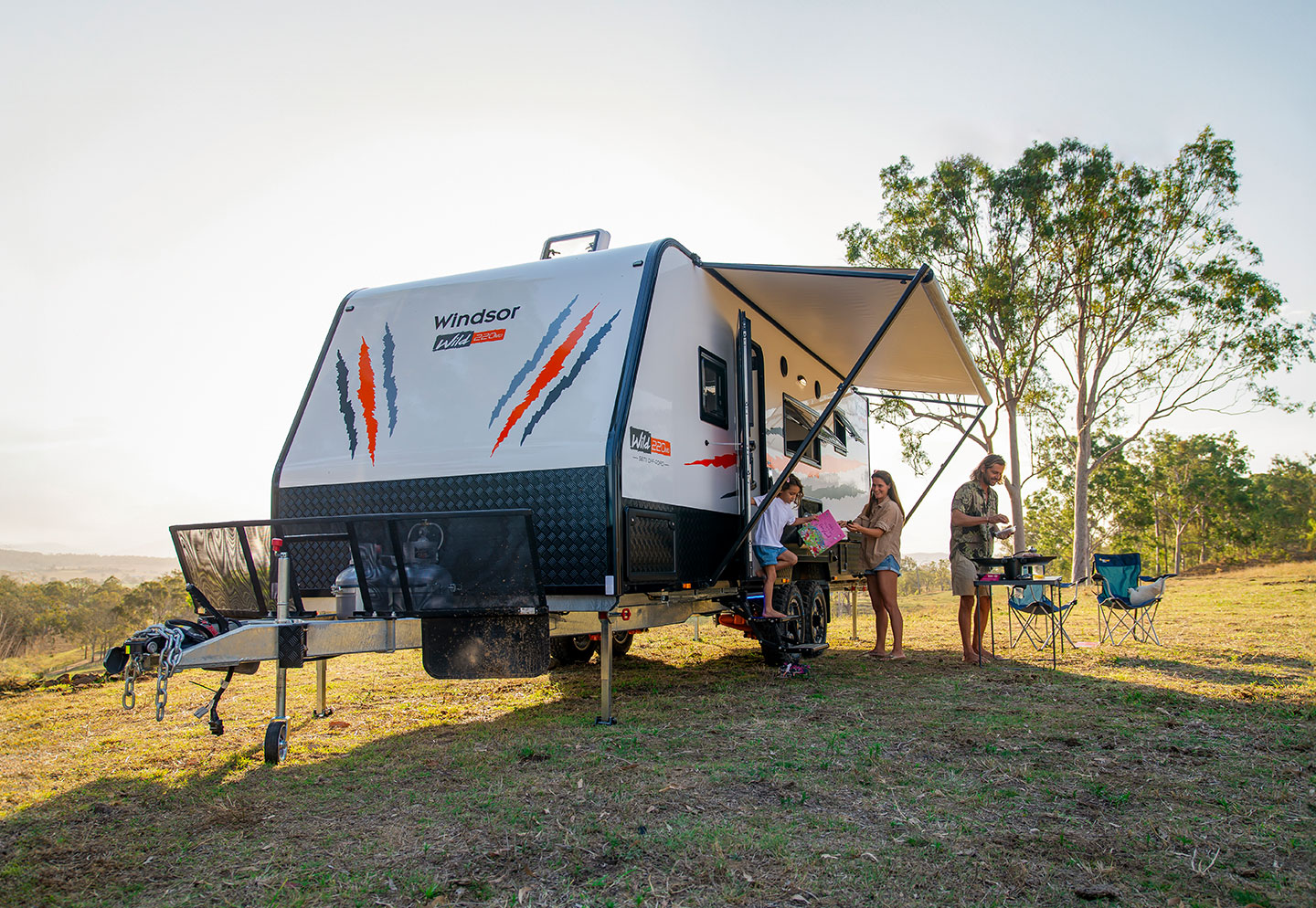 Family outside a wild caravan parked in a picturesque landscape, enjoying the natural surroundings and spending quality time together.