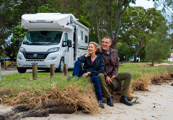 Older couple relaxing on grass in front of a Windsor Flinders motorhome, showcasing Apollo RV Super Centre’s luxury motorhome selection.