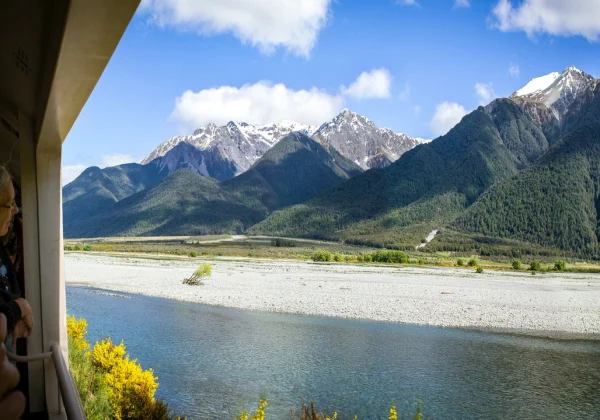 From the carriage of a train looking at snow covered mountains behind a stream