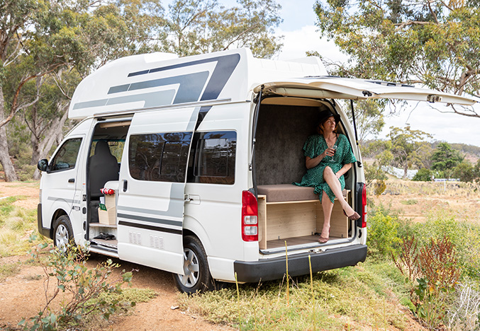 Woman sitting in the back of a used KEA Navigator campervan in outback bushland, highlighting Apollo RV Super Centre's range of preowned RVs and caravans.