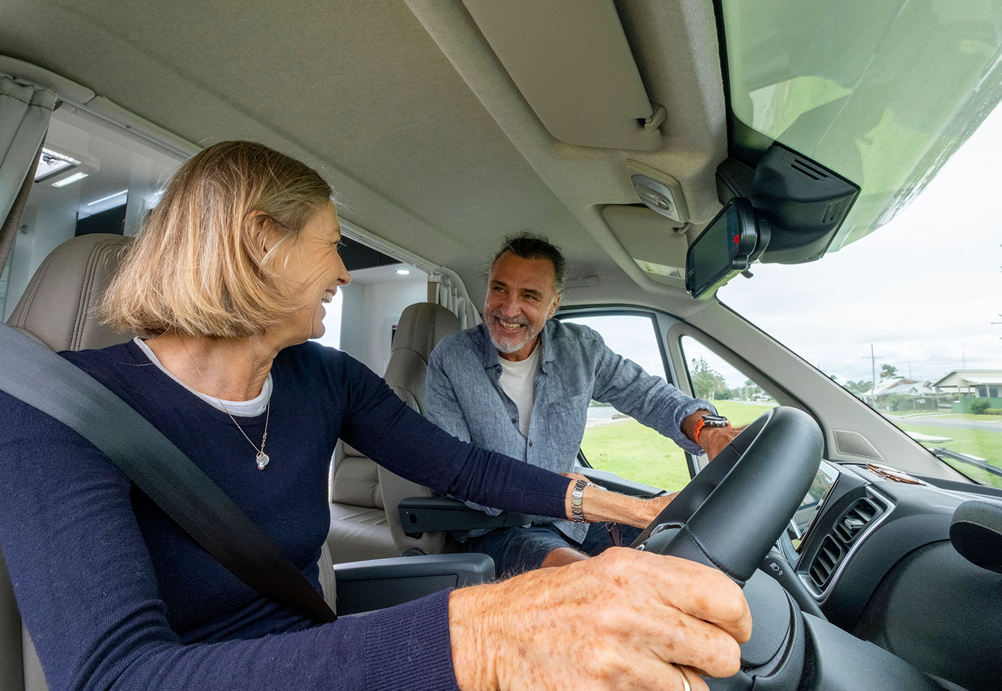 Inside view of a motorhome with a couple driving, showcasing the interior dashboard and their engagement in the journey.