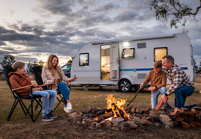 Family around a campfire at sunset with an Adria Altea caravan, showcasing Apollo RV Super Centre's quality caravans.