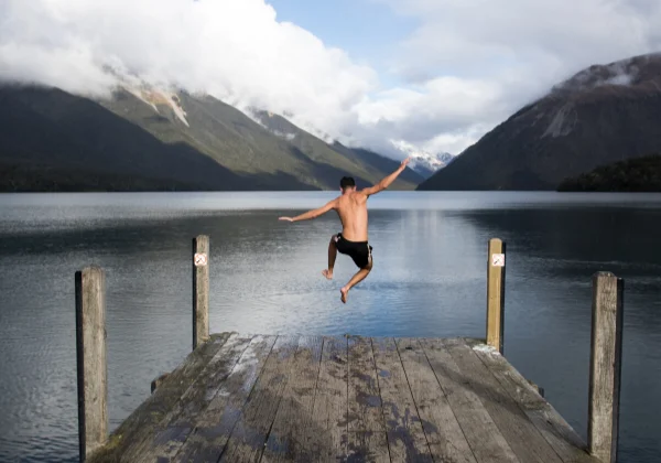 Man running off the end of a wharf about to jump into a lake surrounded by mountains