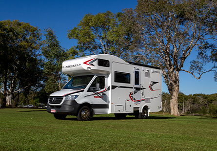 Winnebago Cottesloe Motorhome parked on green grass in front of a tree, clear blue skies in background.