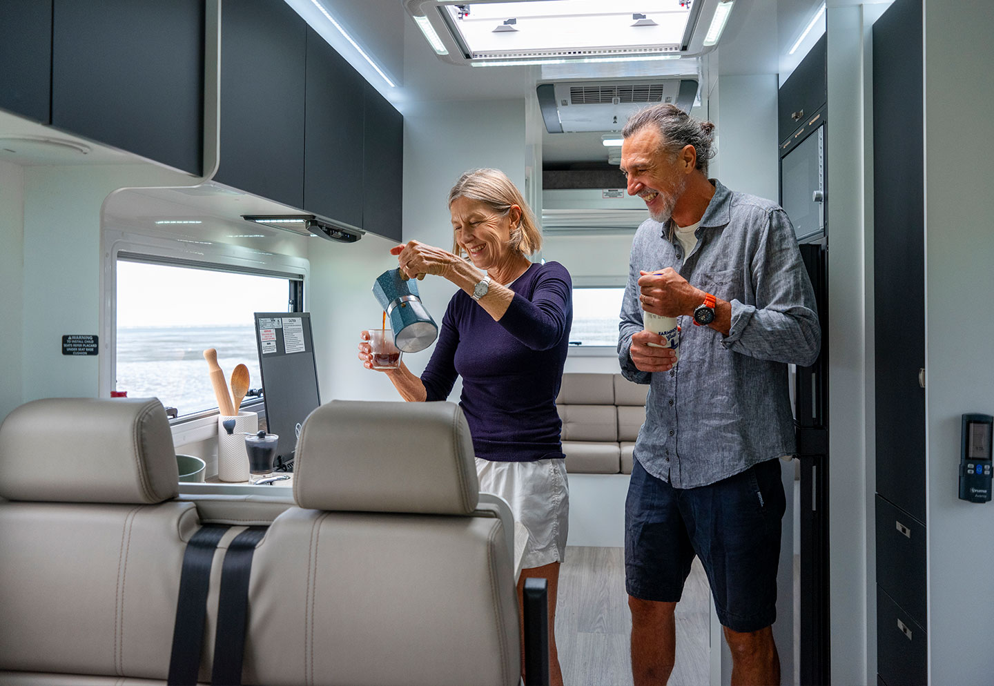 Couple cooking inside a motorhome, using the kitchen amenities and preparing a meal together in a compact space