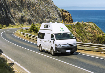 A KEA Hitop Campervan drives along a winding cliffside road, offering stunning views of the ocean below.