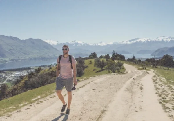 Man walking away from a lake and snowy mountains