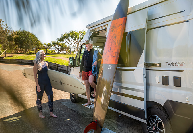 Older couple with surfboards exiting an Adria Twin Campervan, highlighting Apollo RV Super Centre's campervans for easy Australian adventures.