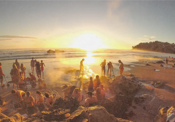 People sitting in small dug out pools in the beach, enjoying the naturally hot water while the sun sets 