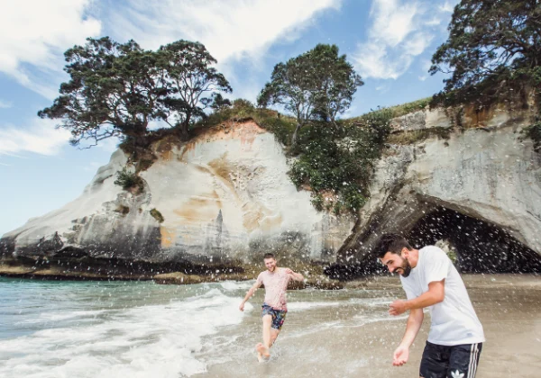 Two friends water fighting in a bay with a cliff in the background