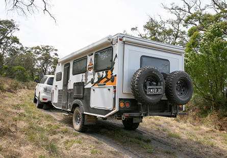 A Lumberjack Buffalo Hybrid camper trailer being towed behind a white SUV uphill on a dirt 4WD track.