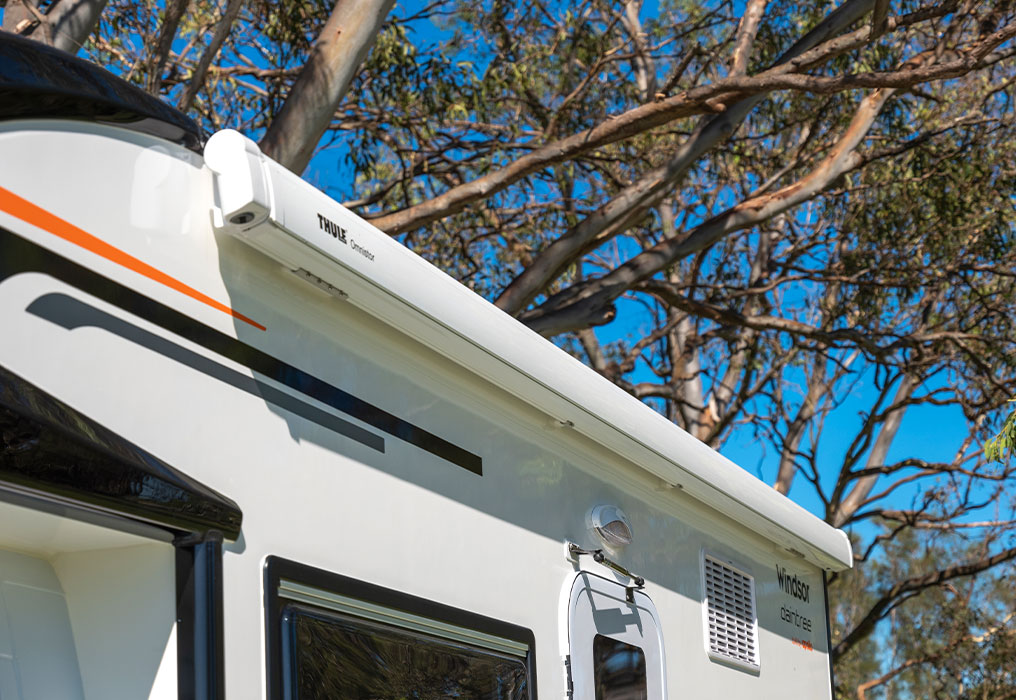 Caravan with an awning, roof hatch, and screened security door, highlighting outdoor comfort and security features.