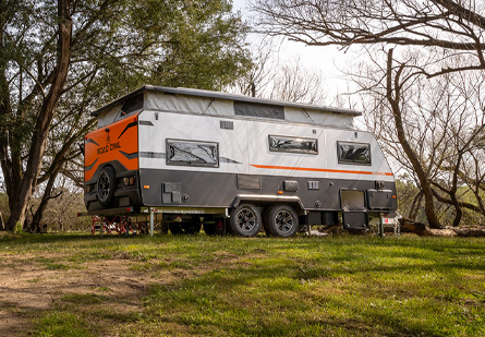 A New Age Caravan with pop top extended in a grassy secluded camping setup.