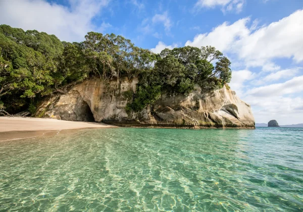 Ocean, white sand with cliff face that has a large hole above the sand and water