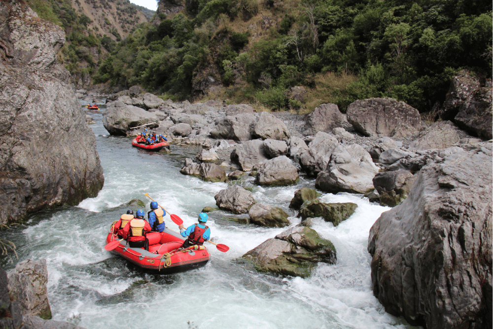 5 people rafting down a river with safety gear
