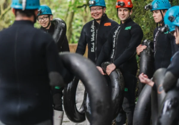 People preparing to go black water rafting, in wet suits holding rubber floating tubes