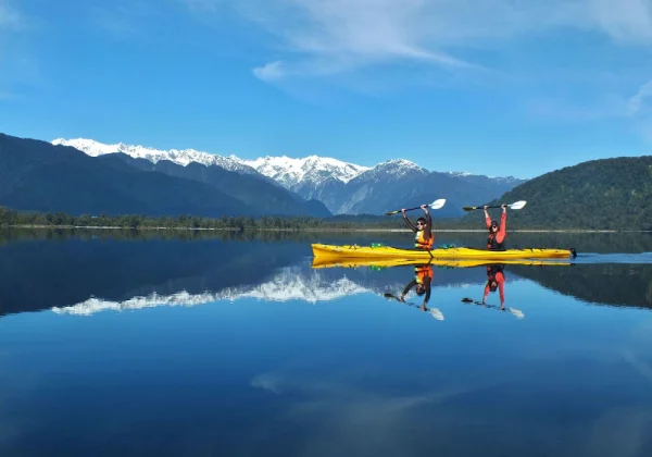 Kayakers on a very still lake reflecting the snowy mountains