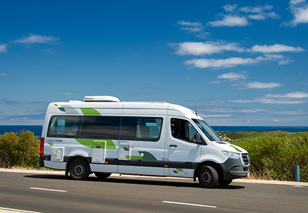 A KEA Nomad Campervan is parked on a scenic oceanside road, with the ocean in the background. The campervan's sleek design and vibrant colors blend with the coastal landscape.