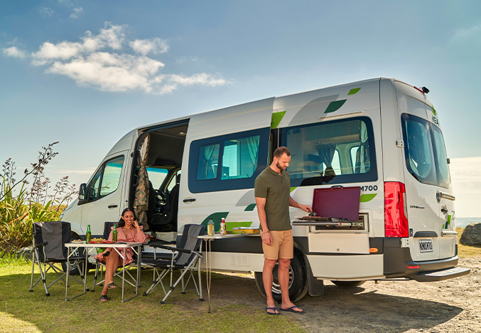 Couple with a small camping set up, cooking a meal with a KEA Campervan