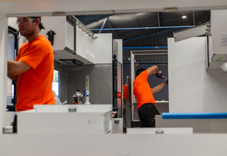 Inside view of a motorhome during the manufacturing process, showing workers assembling components and the partially constructed interior