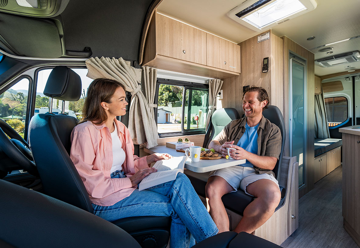 Couple Sitting on the inside dining area of their Winnebago Campervan