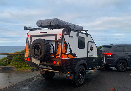 A Lumberjack Sorrento camper trailer being towed behind a black SUV vehicle.