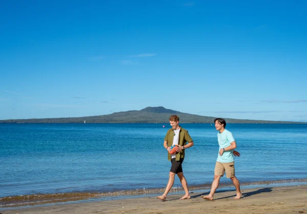 Friends walking along the beach with the volcanic island Rangitoto in the background